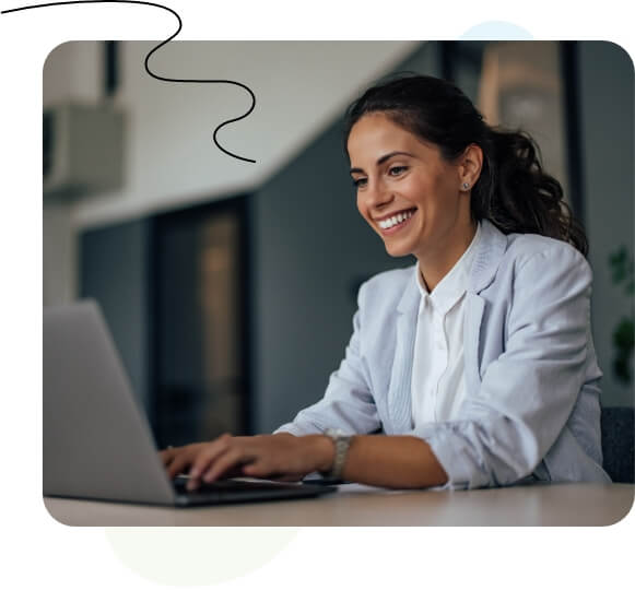 Una mujer sentada en un escritorio, escribiendo en una computadora portátil frente a una pizarra.