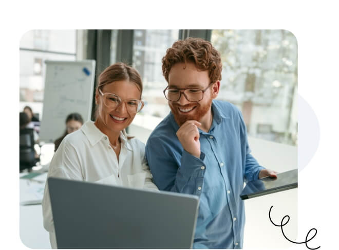 Un hombre y una mujer felices con gafas sonriendo ante la misma computadora portátil.